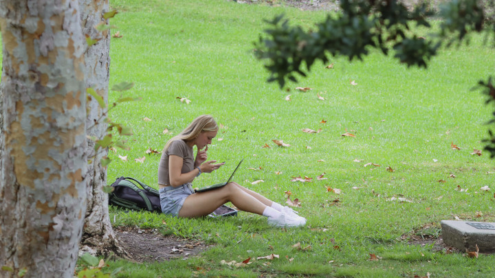 A student sitting on grass with their laptop on their lap.